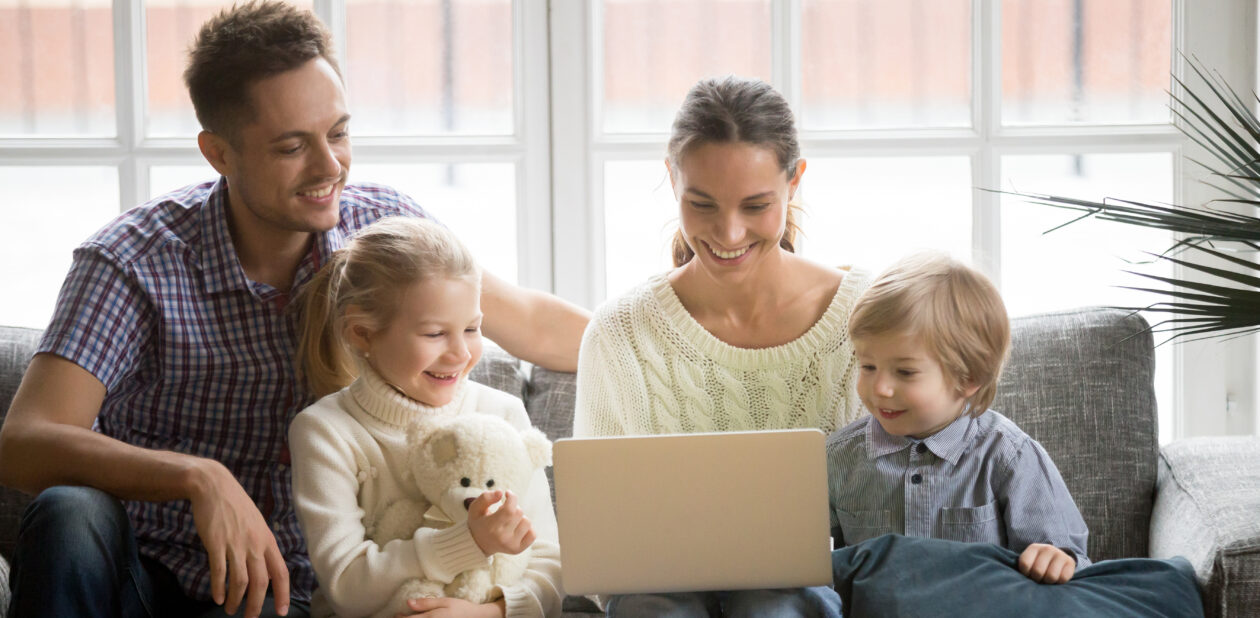 Happy family with children having fun using laptop on sofa